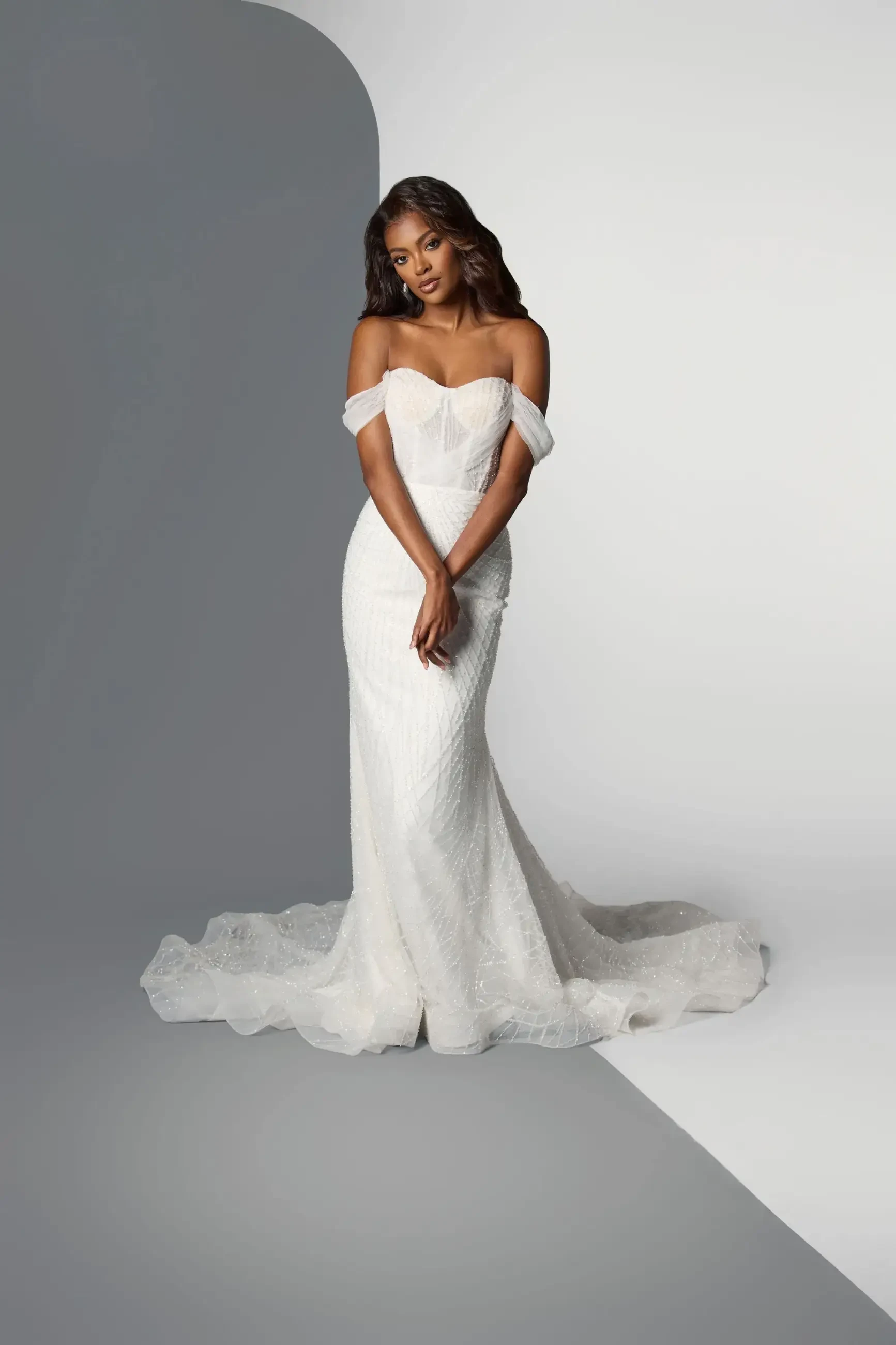 Model is wearing an off-the-shoulder fit-and-flare wedding dress with a corset bodice and train.