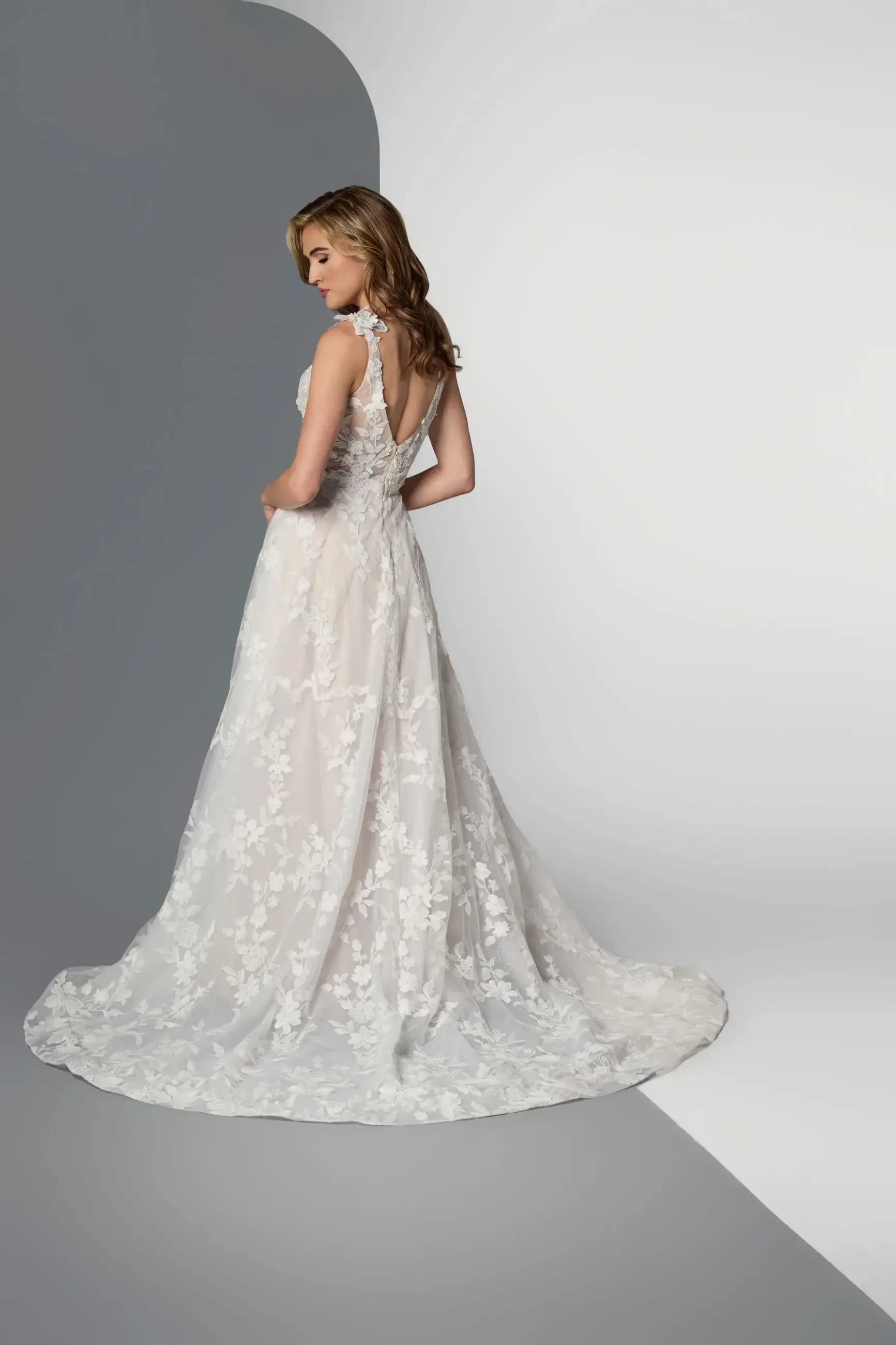 Model is wearing a sleeveless A-line wedding dress with floral lace and a plunging neckline.