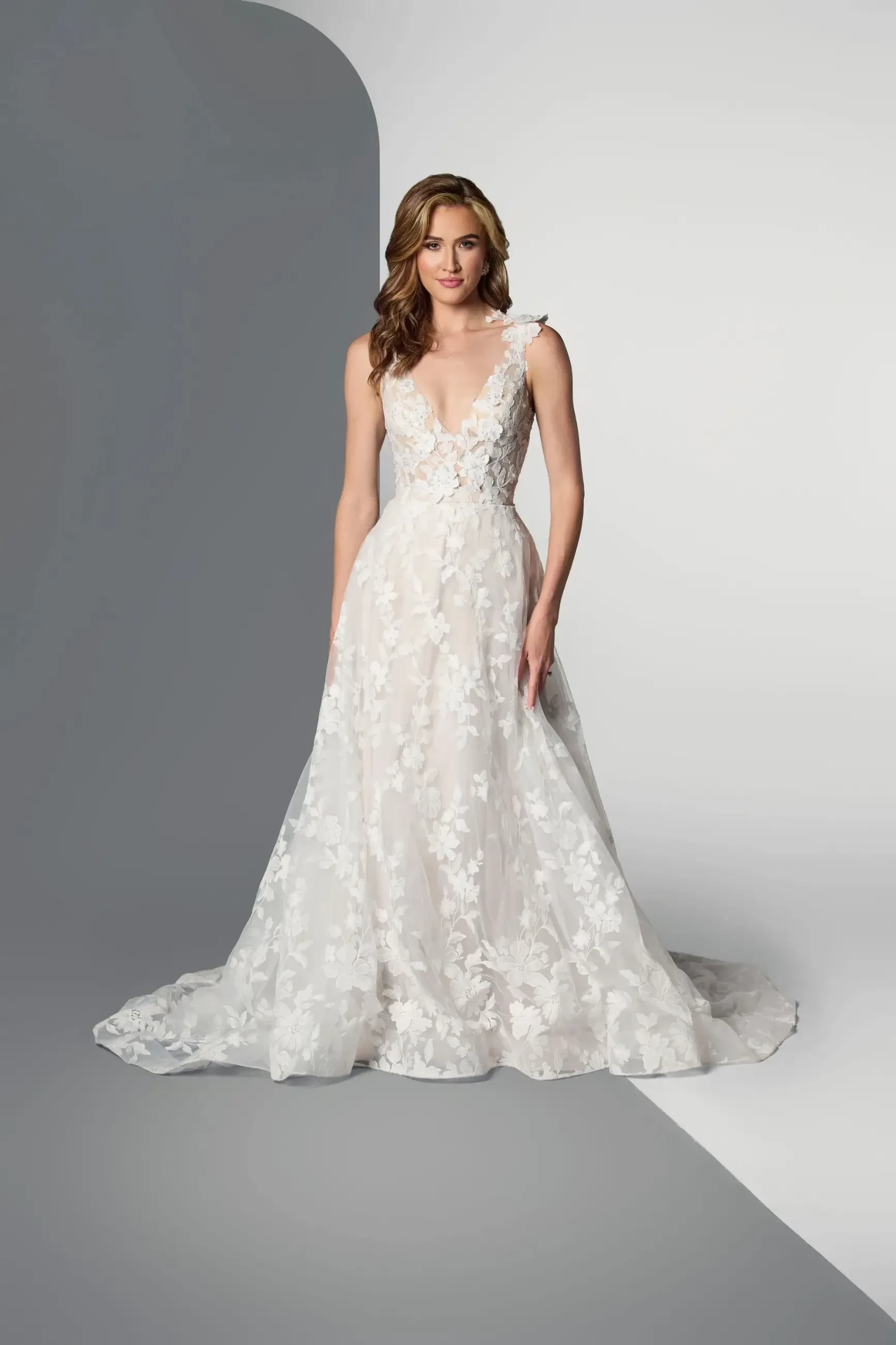 Model is wearing a sleeveless A-line wedding dress with floral lace and a plunging neckline.