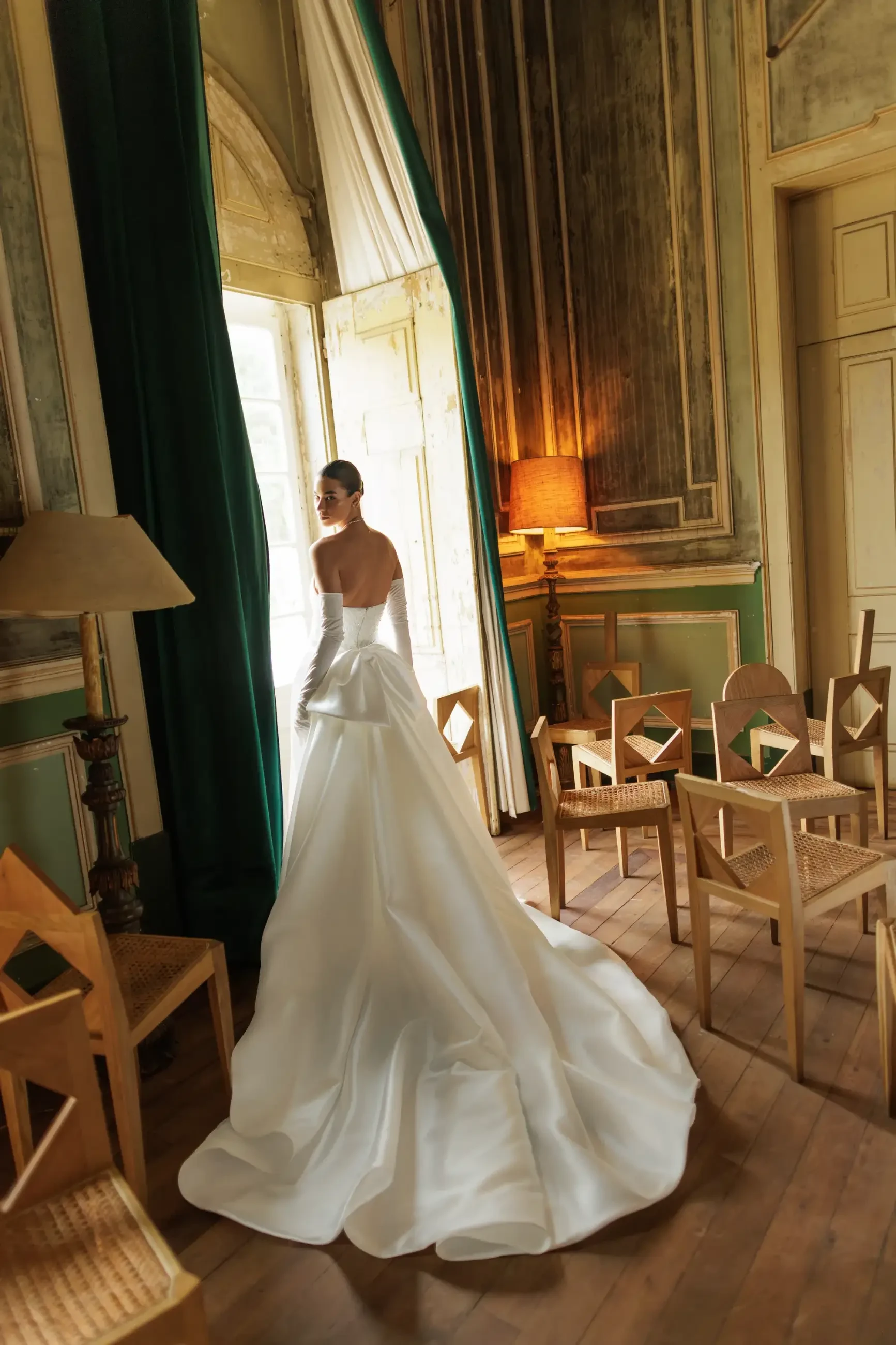 Model is wearing a boat neckline wedding dress with a detachable satin infinity bow