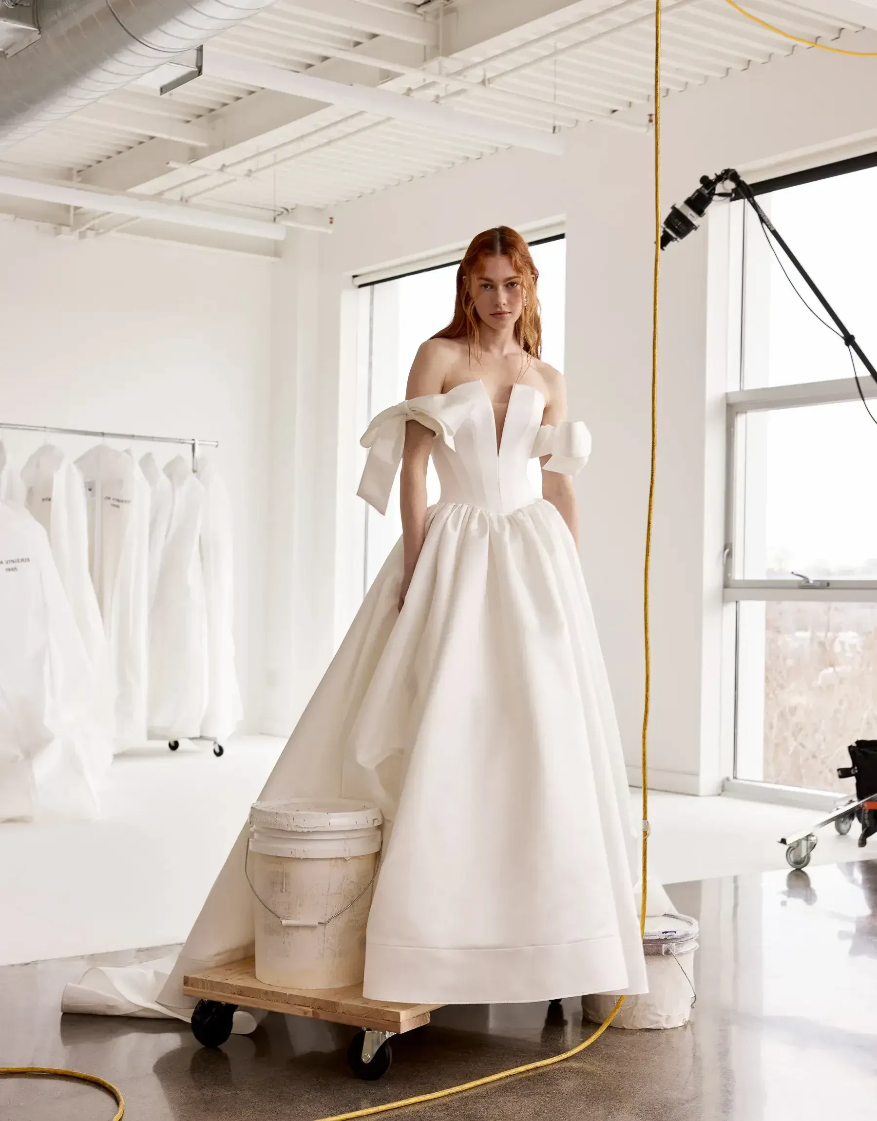 Model is wearing an off the shoulder ball gown wedding dress with a plunging neckline and oversized bows on the sleeves 
