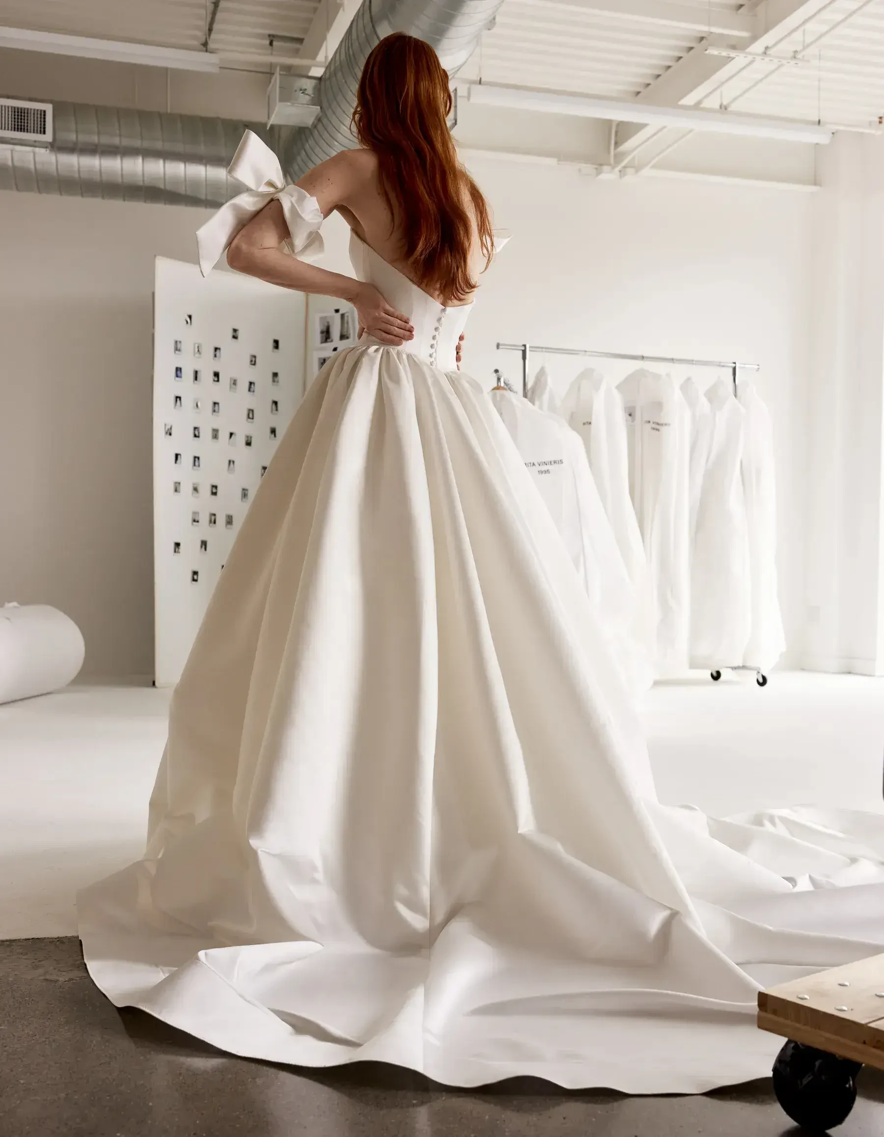 Model is wearing an off the shoulder ball gown wedding dress with a plunging neckline and oversized bows on the sleeves 