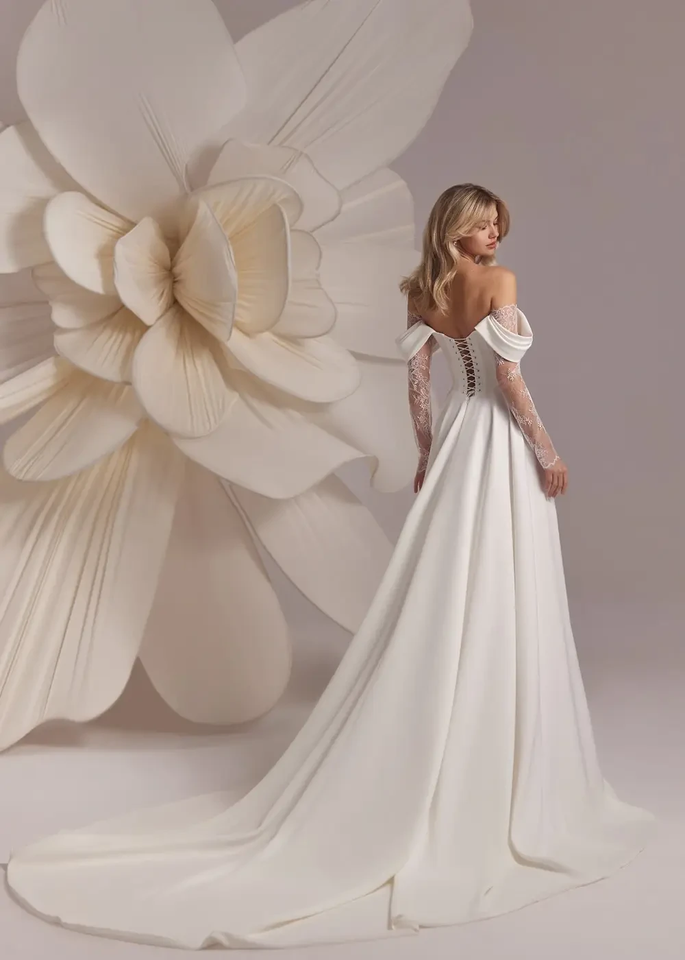 Model is wearing an off the shoulder a-line bridal gown with lace sleeves and a split overskirt 