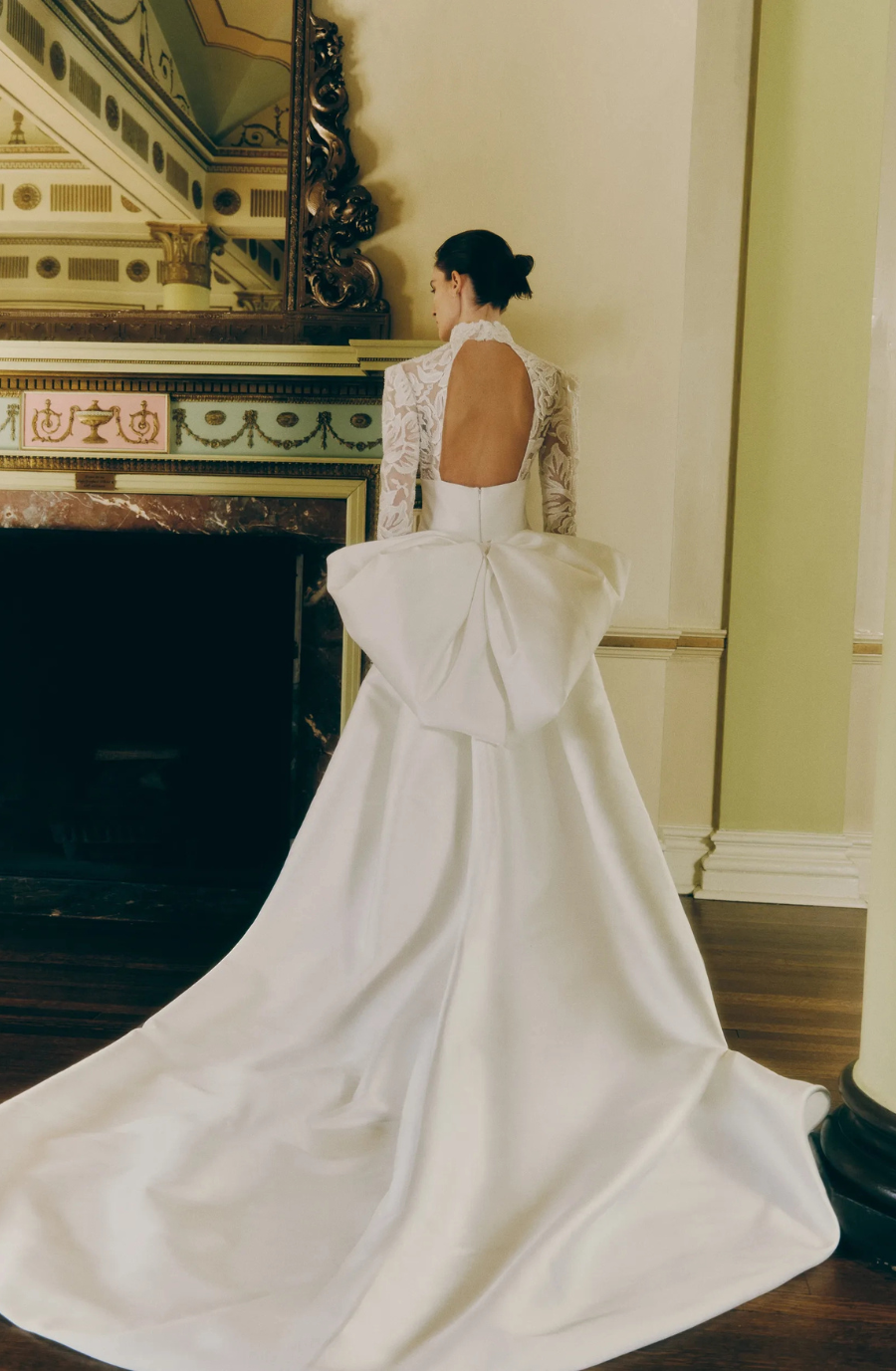 model is wearing a high neck long sleeve ball gown with an open back